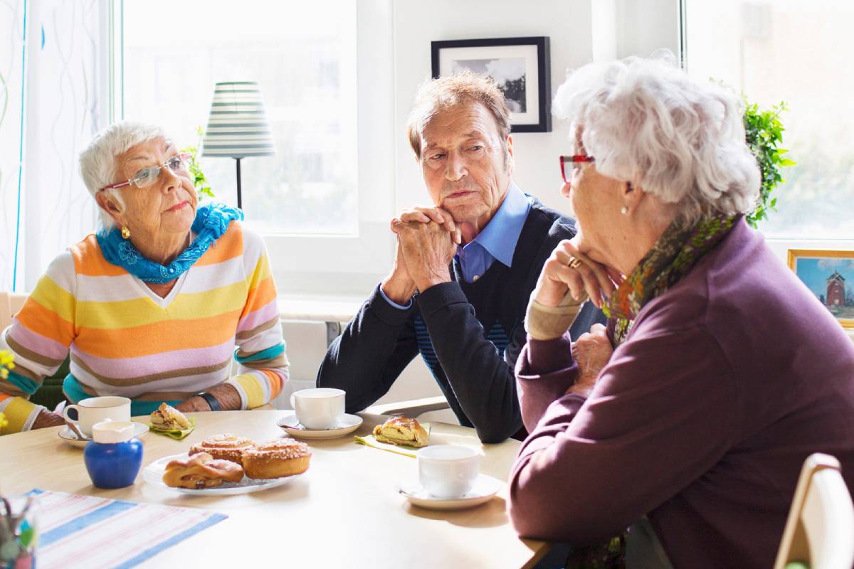 Tre äldre personer sitter och fikar.
