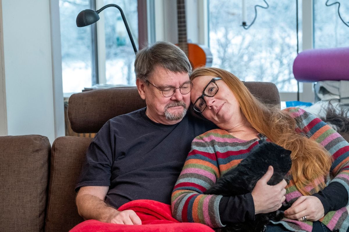 En man och en kvinna sitter i en soffa och håller om varandra. I kvinnans knä sitter en katt.