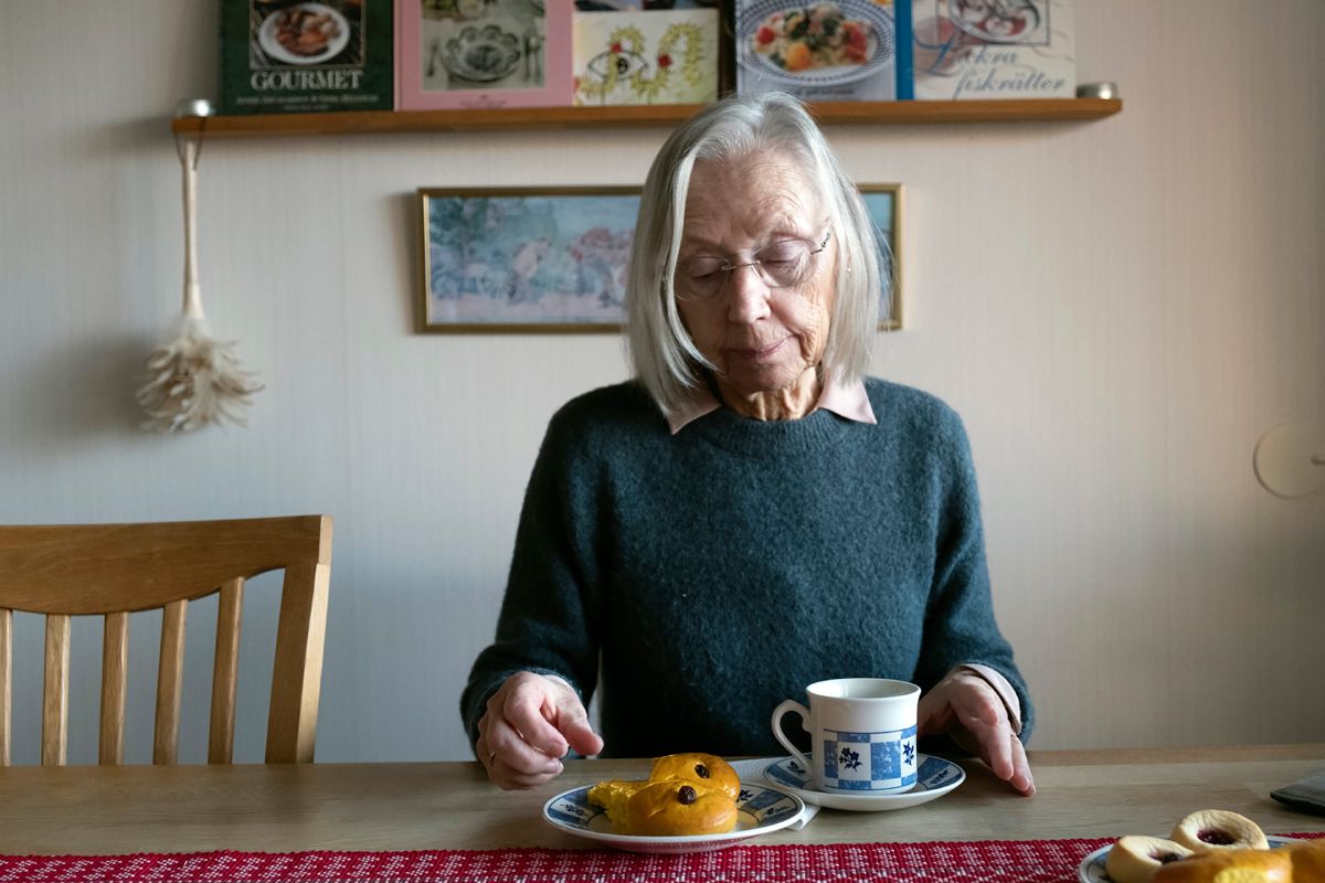 En kvinna sitter vid ett köksbord och fikar.