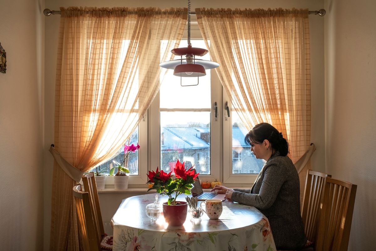 En kvinna sitter framför datorn vid ett köksbord.