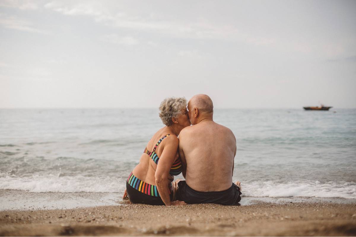 Ett äldre par sitter på stranden och kysser varandra.